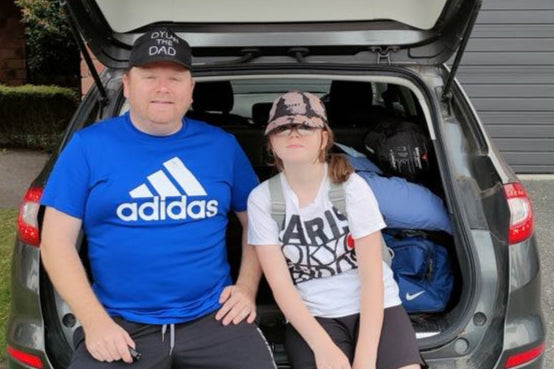 Two people sitting in the open trunk of a car, the male with a DYLAN THE DAD home made cap.